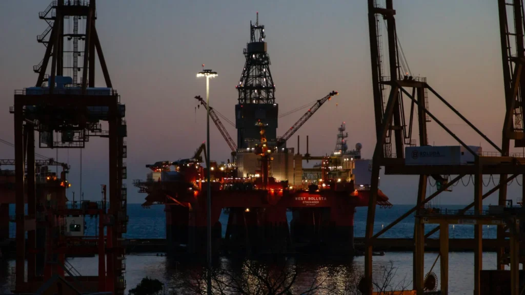 Offshore oil rig silhouette at sunset with a red downward trend arrow breaking an oil barrel for UAE OPEC exit analysis
